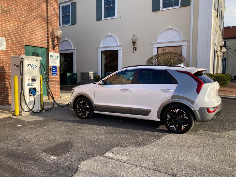 A white Kia Niro EV charges at an EVgo charging station parking lot.