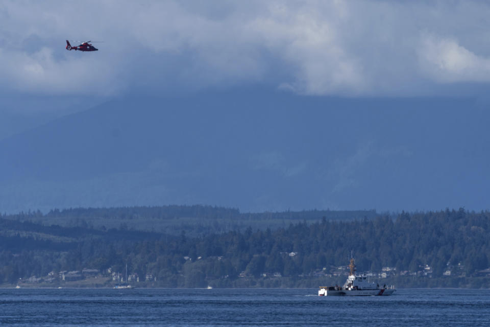 A U.S. Coast Guard boat and helicopter search the area Monday, Sept. 5, 2022, near Freeland, Wash., on Whidbey Island north of Seattle where a chartered floatplane crashed the day before. The plane was carrying 10 people and was en route from Friday Harbor, Wash., to Renton, Wash. (AP Photo/Stephen Brashear)