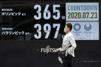 A man wearing a mask against the spread of the new coronavirus walks in front of a countdown calendar showing 356 day to start Tokyo 2020 Olympics and 397 days for Paralympics Thursday, July 23, 2020, in Tokyo. The postponed Tokyo Olympics have again reached the one-year-to-go mark. But the celebration is small this time with more questions than answers about how the Olympics can happen in the middle of a pandemic. That was before COVID-19 postponed the Olympics and pushed back the opening to July 23, 2021. (AP Photo/Eugene Hoshiko)