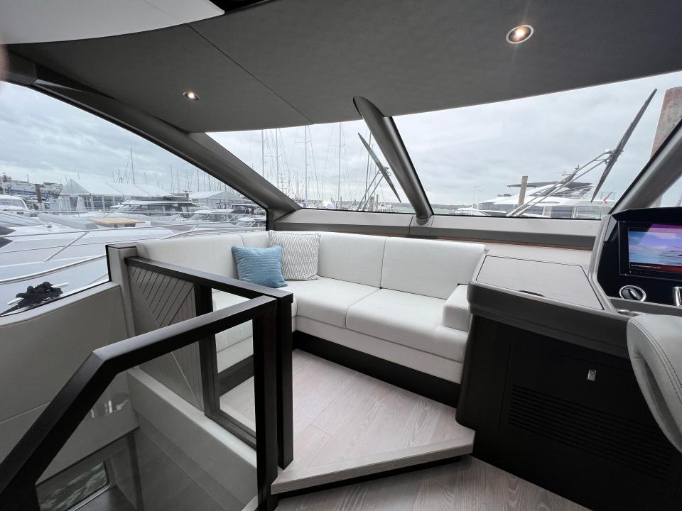 A l-shaped couch next to the console underneath vast windshield of Sunseeker 76 yacht