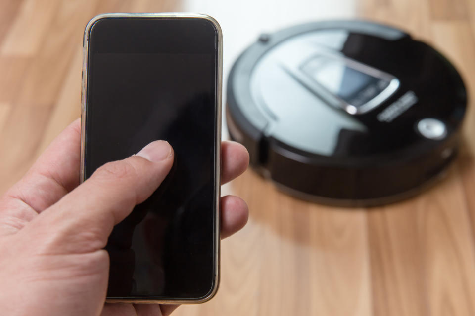 A hand holding a smartphone controlling a robotic vacuum cleaner.