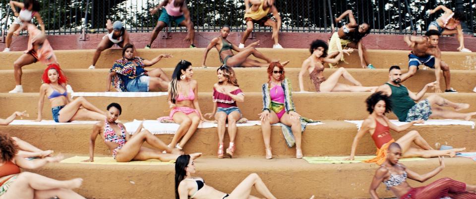 Stephanie Beatriz, Daphne Rubin-Vega, and Dascha Polanco sit amid posing sunbathers near a pool