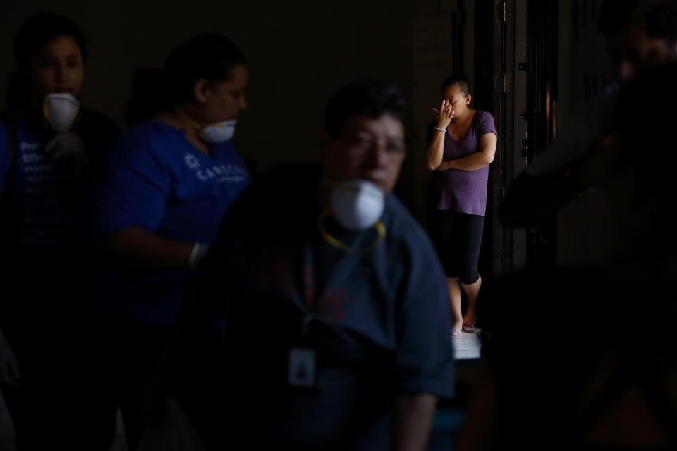 In this Oct. 26, 2019, photo, a woman waits by the door as volunteer health practitioners set up a clinic in a shelter for migrants in Tijuana, Mexico. A burgeoning grassroots movement of health professionals and medical students from both sides of the U.S.-Mexico border is quietly battling on the front lines to keep asylum seekers healthy and safe. It is a daunting task taken on by volunteers trying to desperately tend to a need left largely unmet by the governments of both countries. (AP Photo/Gregory Bull)