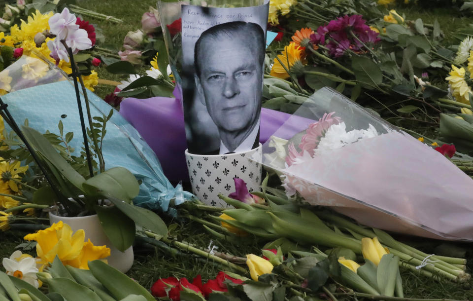 A photo of Britain's Prince Philip is among flowers left by the public outside the gates of Windsor Castle, a day after the death of Britain's Prince Philip, in Windsor, England, Saturday, April 10, 2021. Britain's Prince Philip, the irascible and tough-minded husband of Queen Elizabeth II who spent more than seven decades supporting his wife in a role that mostly defined his life, died on Friday. (AP Photo/Frank Augstein)