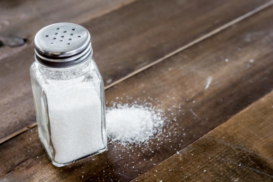 salt shaker next to some spilled salt on a wooden table