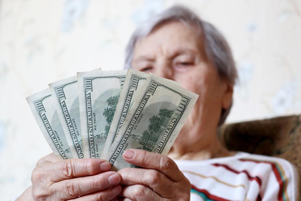 A person sitting in a chair counting a fanned pile of one hundred dollar bills in their hands. 