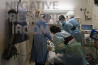 FILE - In this Nov. 19, 2020, file photo, EMT Giselle Dorgalli, second from right, looks at a monitor while performing chest compression on a patient who tested positive for coronavirus in the emergency room at Providence Holy Cross Medical Center in the Mission Hills section of Los Angeles. Amid the coronavirus resurgence, states have begun reopening field hospitals to handle an influx of sick patients that is pushing health care systems — and their workers — to the breaking point. Hospitals are bringing in mobile morgues. And funerals are once again being livestreamed or performed as drive-by affairs. (AP Photo/Jae C. Hong, File)