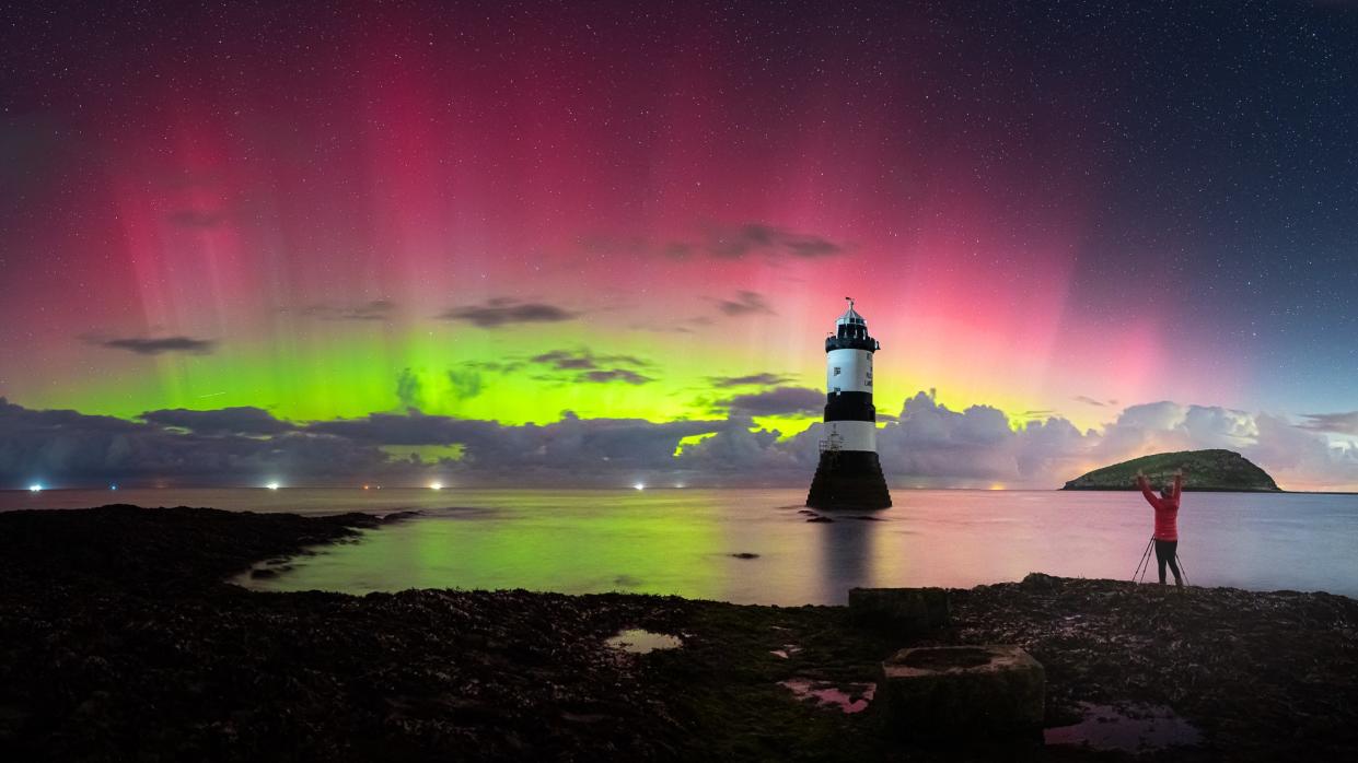  Vibrant green and red pillars of light in the sky above a lighthouse. . 