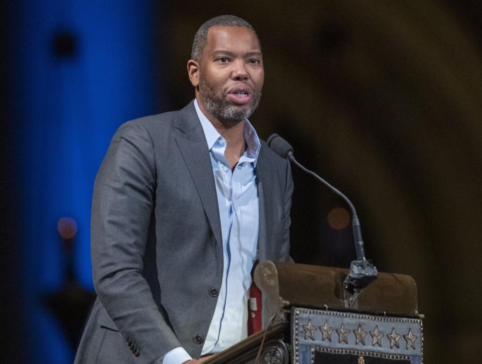 A man in a suit coat and button-down shirt speaks into a microphone at a lectern.