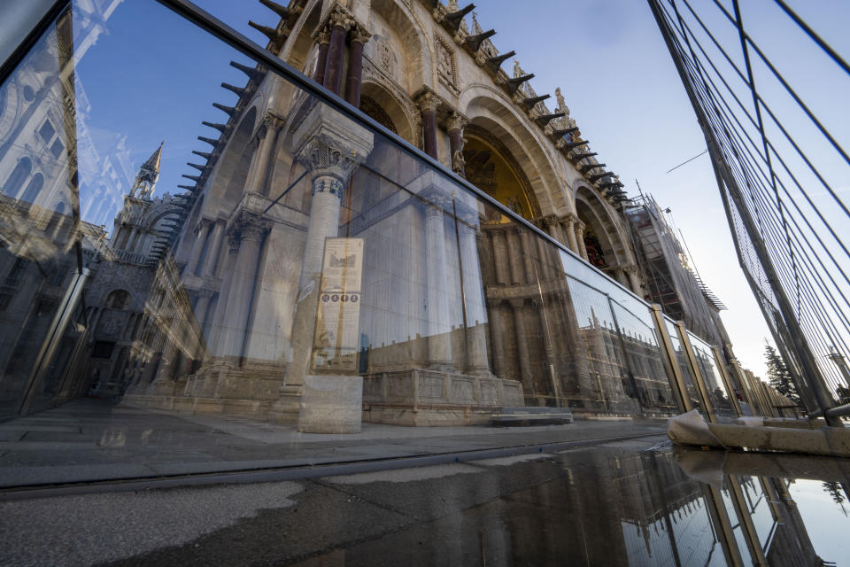 A thin layer of seawater surfaces during a moderately high tide in St. Mark's Square in Venice, northern Italy, Wednesday, Dec. 7, 2022, where glass barriers that prevent seawater from flooding 900-year-old iconic St Mark's Basilica, seen in the background, have been recently installed. St. Mark's Square is the lowest-laying city area and frequently ends up underwater during extreme weather. (AP Photo/Domenico Stinellis)