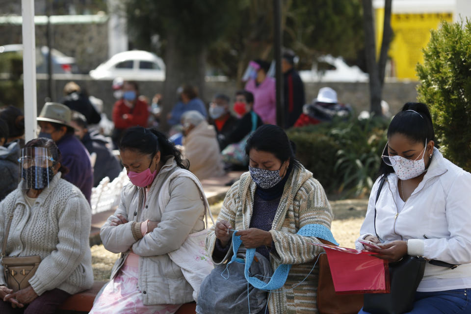 A woman knits as people wait in an hours-long line to get the AstraZeneca vaccine, on the day Mexico began vaccinating its elderly population against COVID-19, outside a health center in the outlying Milpa Alta borough of Mexico City, Monday, Feb. 15, 2021. (AP Photo/Rebecca Blackwell)