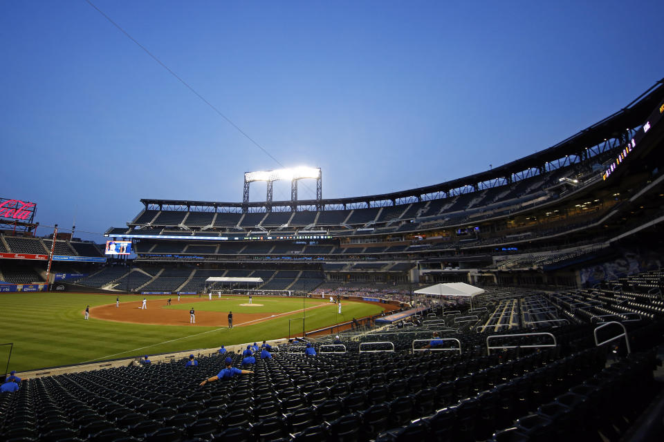 Players for the Mets are in the stands at an empty stadium with the field in front of them.