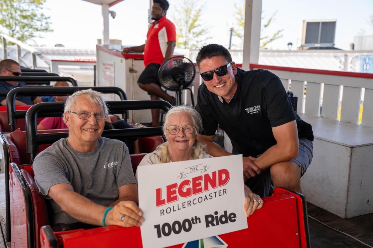 Tom and Margaret Wuggazer hold a 1000th ride sign with Arnolds Park Amusement Park CEO Jon Pausley.