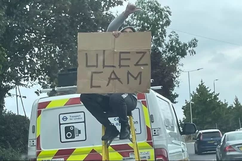 A protestor climbed a ladder to hold a sign blocking a ULEZ camera on top of a van in East London. (Reach)