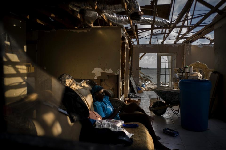 Ebony Thomas looks at her phone a she sits on a sofa inside her shattered home, in the aftermath of Hurricane Dorian, in Mclean's Town, Grand Bahama, Bahamas, Wednesday Sept. 11, 2019. The 15-year-old lost three members of her family to the Hurricane. (AP Photo/Ramon Espinosa)