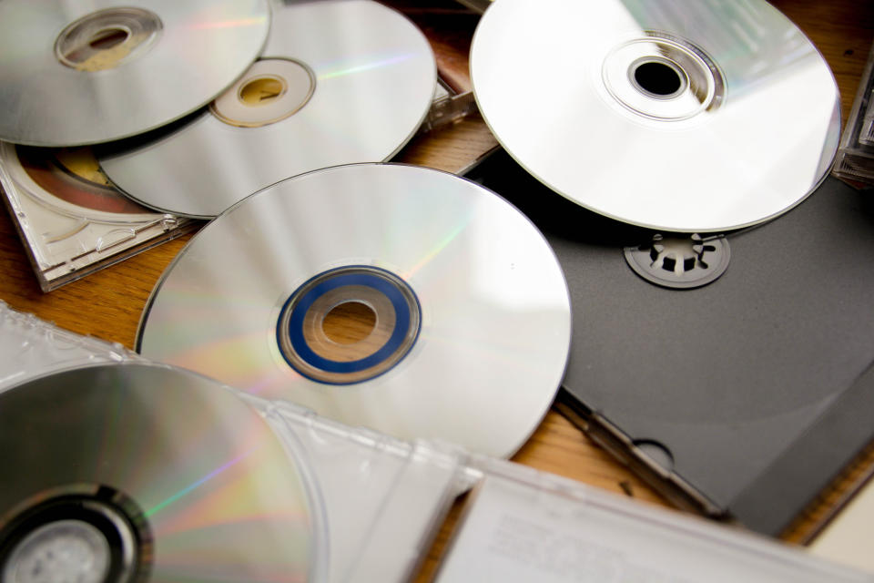 Several CDs scattered on a wooden surface, some in cases, with one inside an open laptop's CD drive