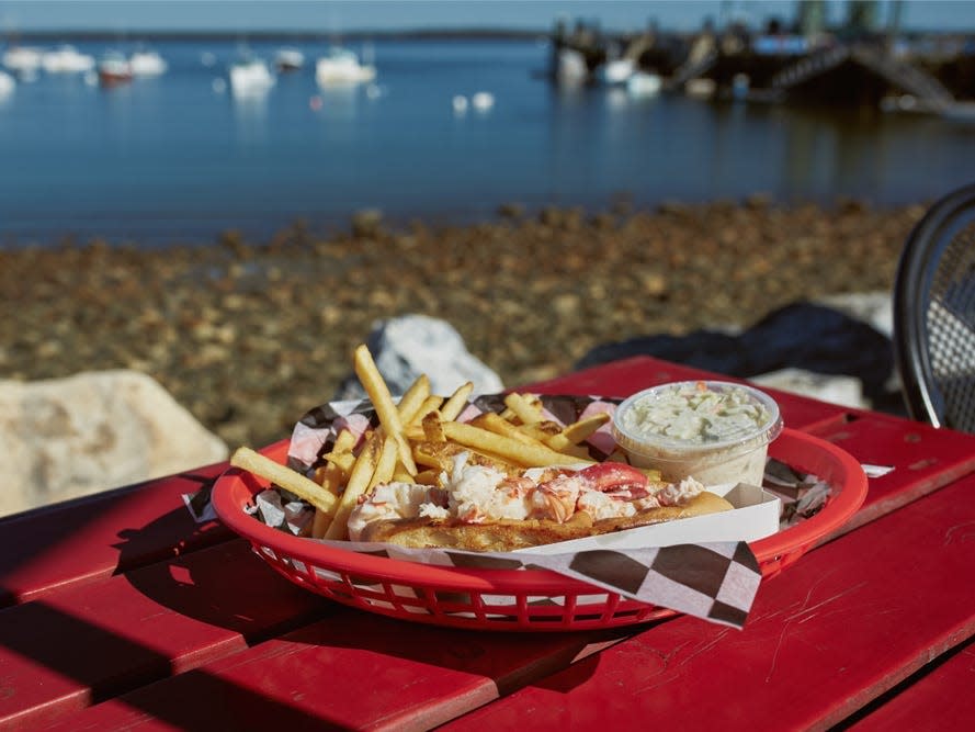 lobster roll in red basket with waterfront harbor in the background