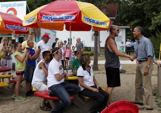 President Barack Obama (R) greets customers before ordering an ice treat at Tropical Sno in Denison, Iowa, while campaigning the state in a luxury bus, August 13, 2012.
