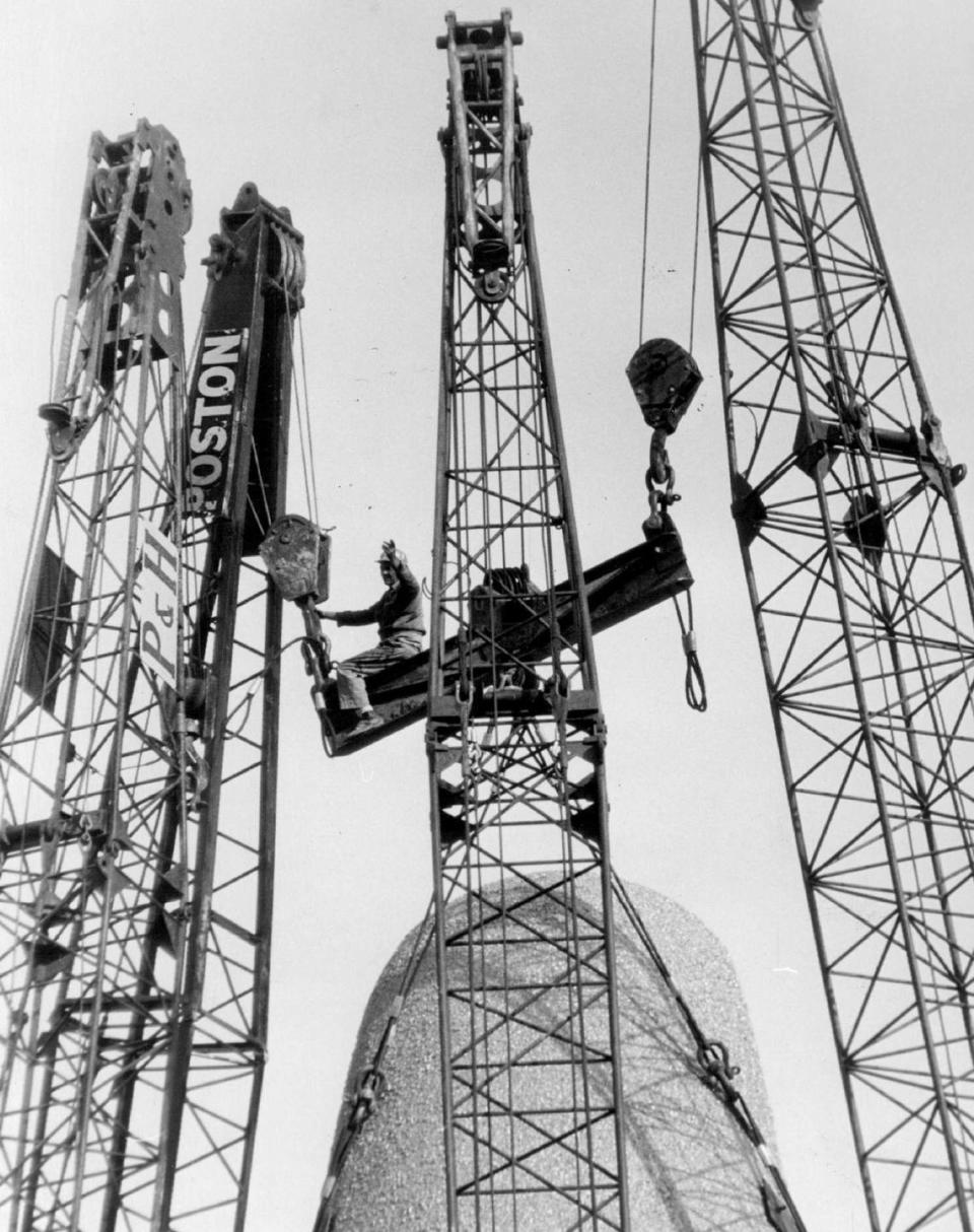 Crews work among steel cranes to anchor the “Arch of Industry” at the Sunshine State Industrial Park. The worker is guiding a steel beam to connect the two 100-ton legs of the arch.