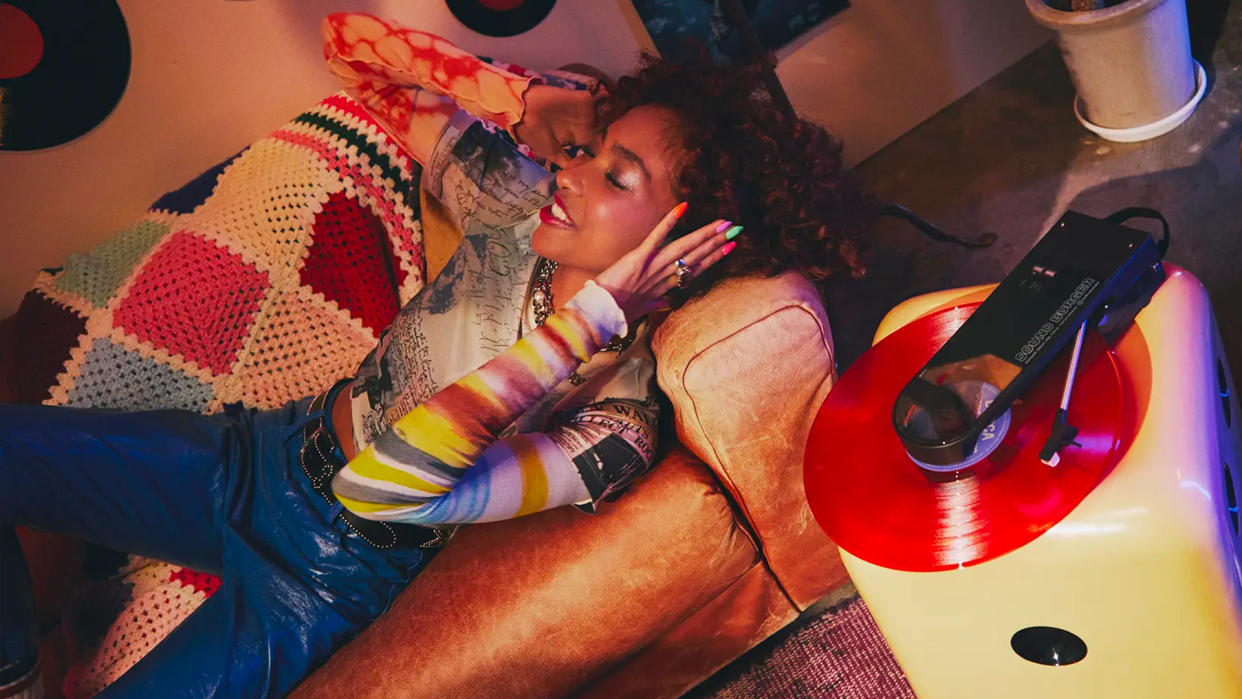  A girl wears headphones while lying on a couch and listening to a record. 