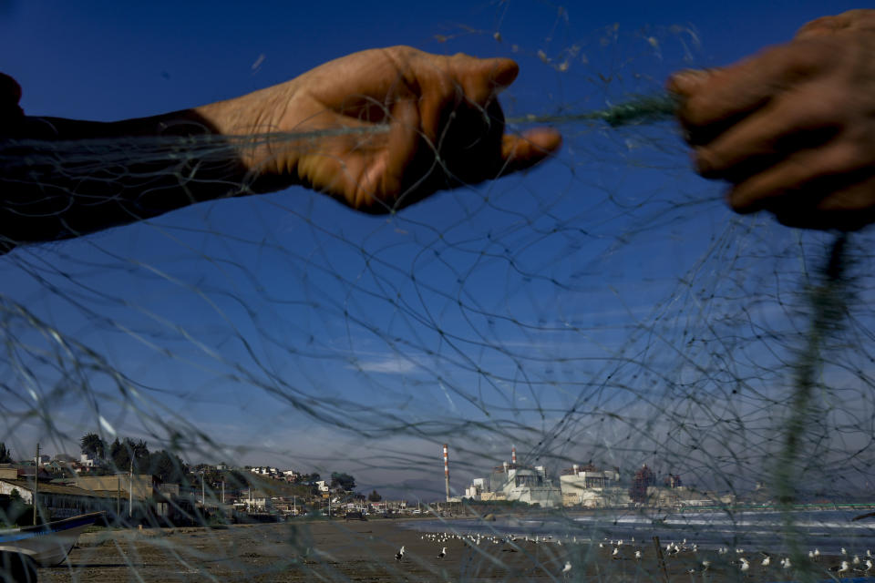 Fishermen work with a net on the beach near the Ventanas Smelter, of the state-owned company Codelco, on the first day of its closure in Quintero Bay in Puchuncavi, Chile, Wednesday, May 31, 2023. Chilean President Gabriel Boric announced in June 2022 the gradual closure of the world's leading copper producer in order to reduce the constant episodes of environmental pollution that affect the coastal communes near the furnace. (AP Photo/Esteban Felix)