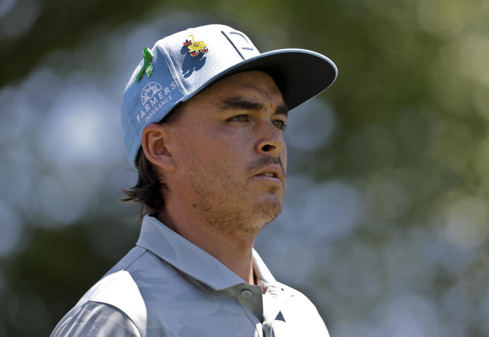 Rickie Fowler wears a green ribbon in support of the victims of the shooting at the University of North Carolina-Charlotte as he walks from the first tee during the first round of the Wells Fargo Championship golf tournament at Quail Hollow Club in Charlotte, N.C., Thursday, May 2, 2019. (AP Photo/Chuck Burton)