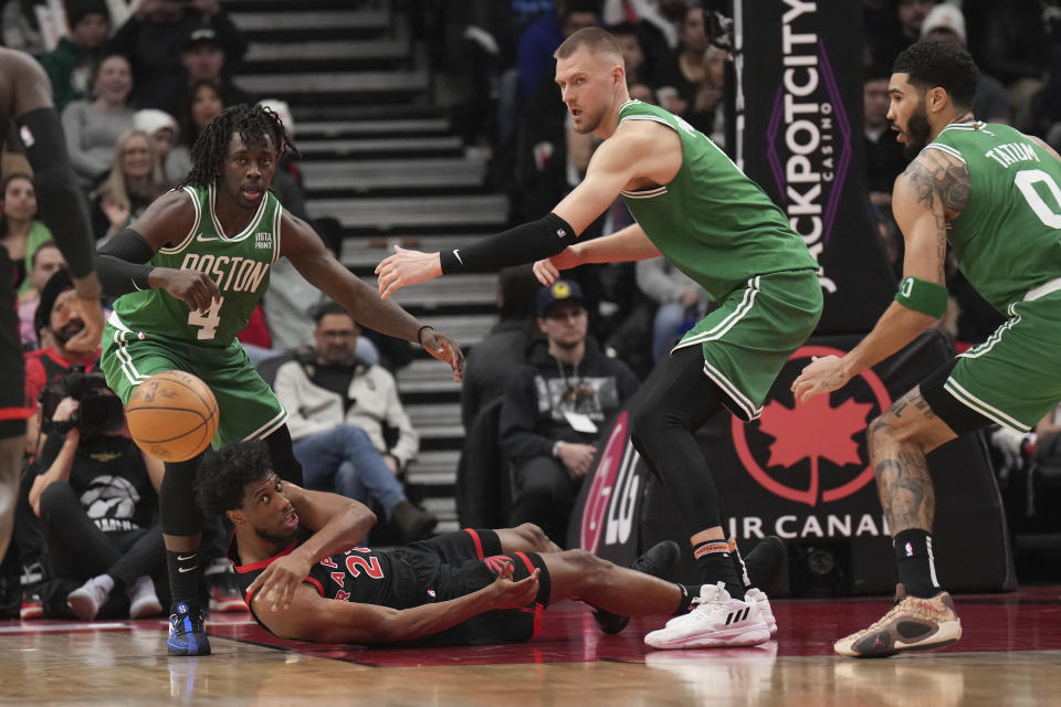 Toronto Raptors forward Thaddeus Young (21) tries to make a pass from the floor as Boston Celtics guard Jrue Holiday (4) and center Kristaps Porzingis, second from right, watch during second-half NBA basketball game action in Toronto, Monday Jan. 15, 2024. (Nathan Denette/The Canadian Press via AP)