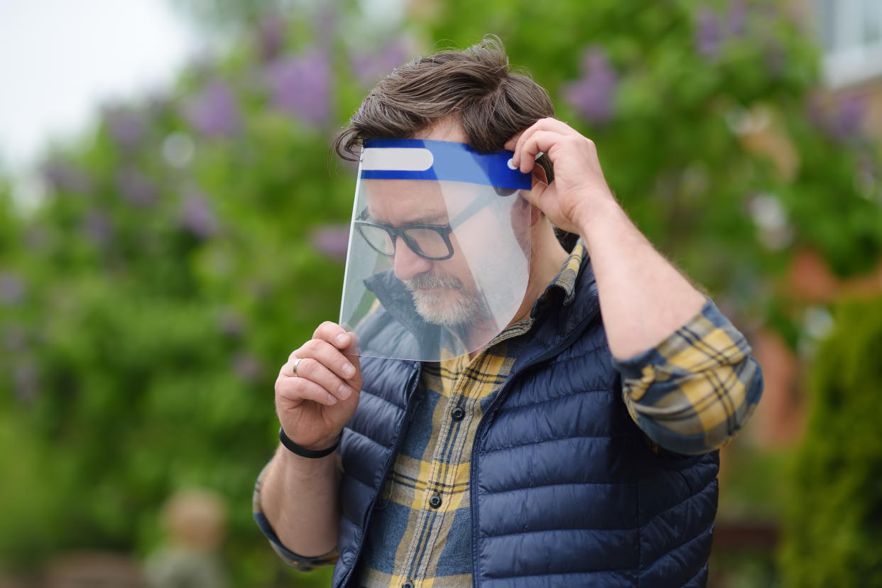 Man putting on face shield on street of city or public park. Safety during COVID-19 outbreak. Lifting virus lockdown. Social distancing and face mask - security measures when exiting quarantine.