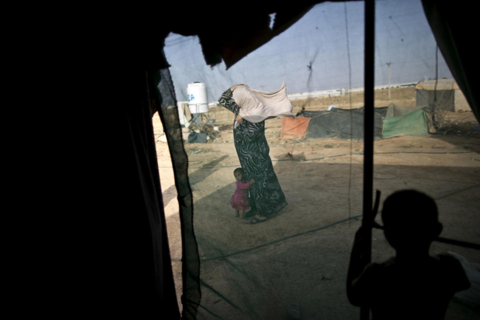 FILE -- In this June 3, 2016 file photo, a Syrian refugee holds on to her headscarf against the wind while she and her daughter stand outside their tent at an informal tented settlement near the Syrian border, on the outskirts of Mafraq, Jordan. Nearly a year after Jordan opened its main border crossing for Syrian refugees to go home, few are taking up the offer. Afraid to return home, unable to earn a decent living in Jordan and unwanted by the West, refugees are trapped in a cycle of poverty and debt while straining the resources of a country that is already struggling to meet the needs of its own population. (AP Photo/Muhammed Muheisen, File)