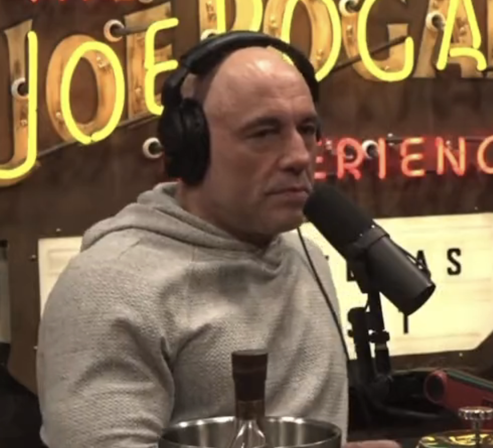 Joe in a hoodie sitting with a microphone, on a podcast set