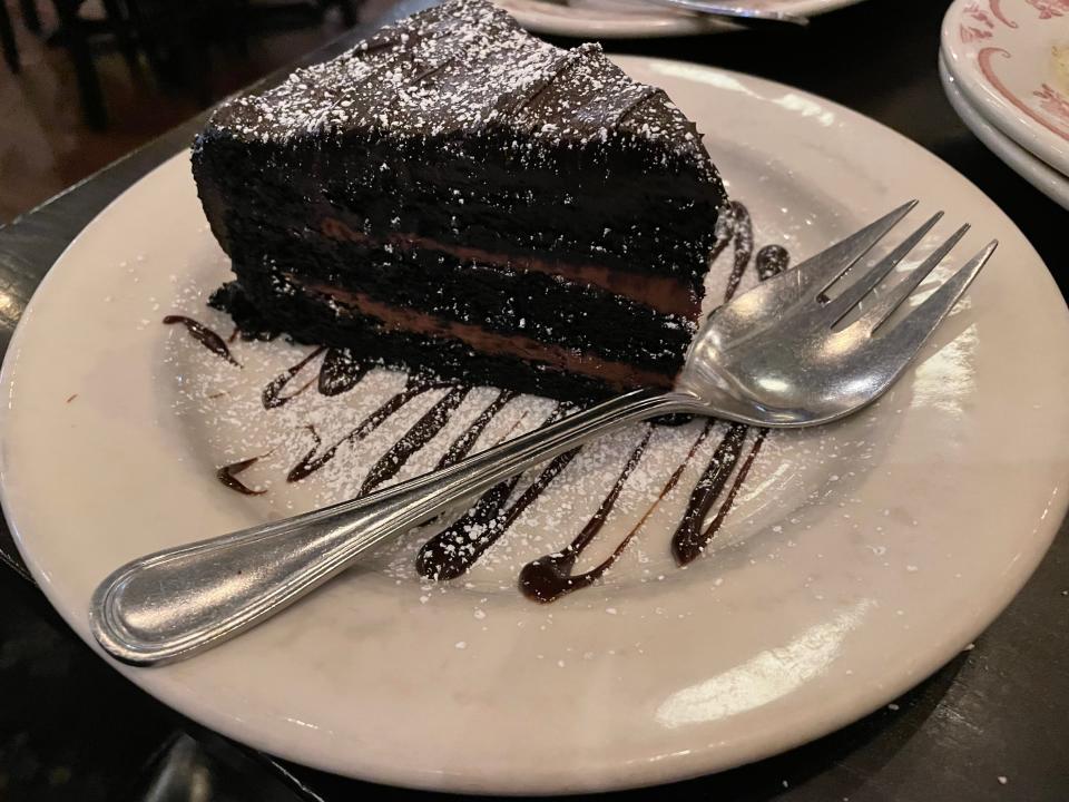 A slice of chocolate cake with distinctive chocolate frosting layers on a white plate drizzled with a chocolate sauce.