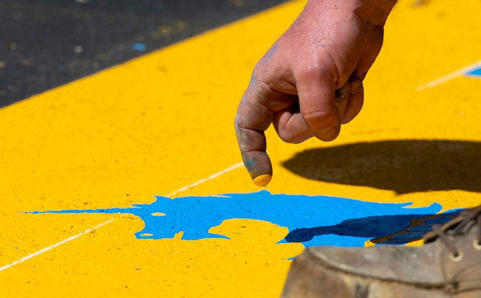 James Sawler, of Road Safe Traffic, literally puts the finishing touch on the start line for the 127th running of the Boston Marathon on Main Street (Route 135) in Hopkinton, creating the unicorn's eyes with his fingertip, April 11, 2023.