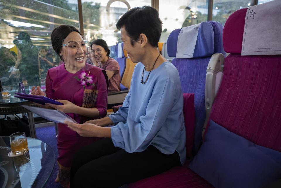 A customer orders meal to a flight attendant in a flight-themed restaurant at the Thai Airways head office in Bangkok, Thailand on Oct. 3, 2020. The airline is selling time on its flight simulators to wannabe pilots while its catering division is serving meals in a flight-themed restaurant complete with airline seats and attentive cabin crew. The airline is trying to boost staff morale, polish its image and bring in a few pennies, even as it juggles preparing to resume international flights while devising a business reorganization plan. (AP Photo/Sakchai Lalit)