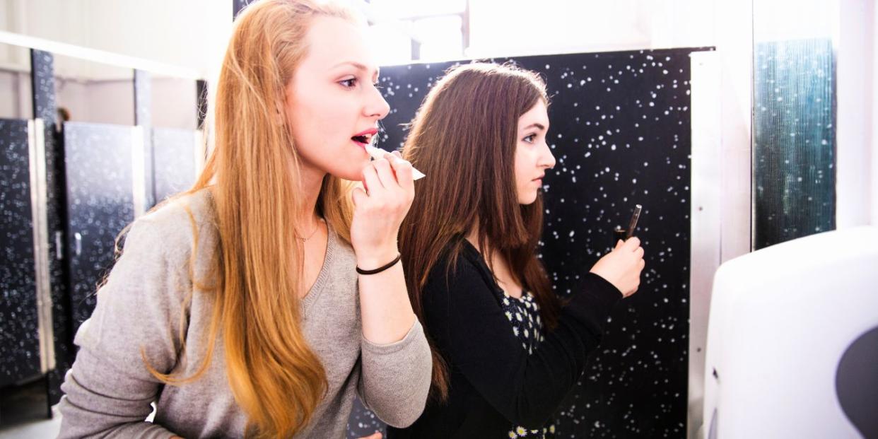 Teen girls using school bathroom mirror