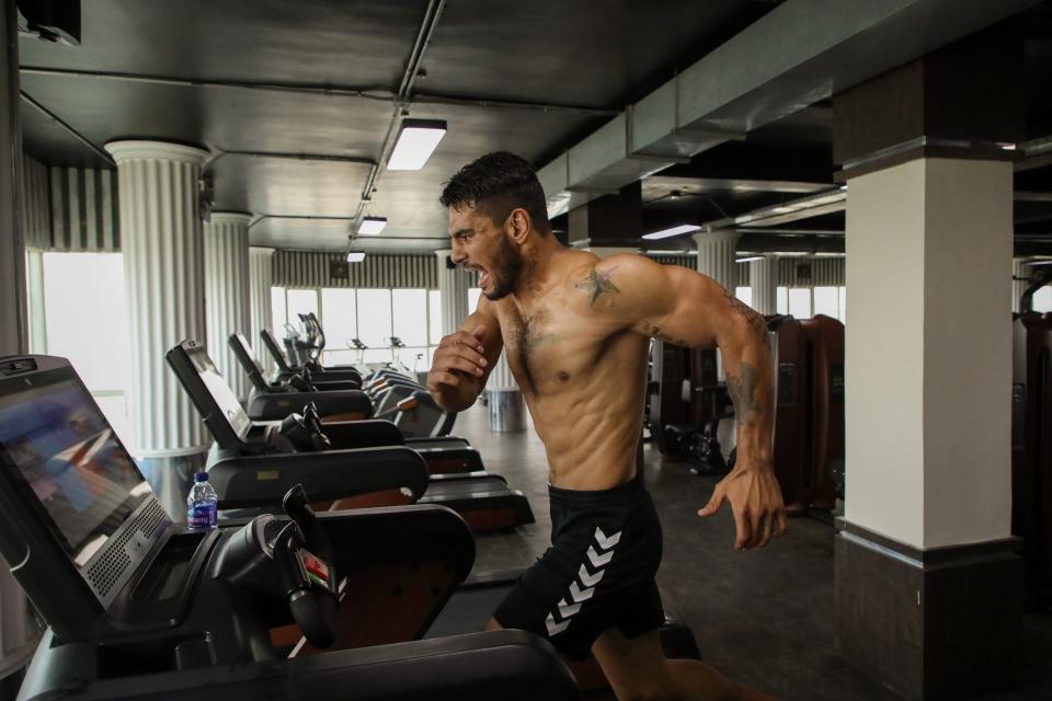 A shirtless man makes faces as he runs on a treadmill.