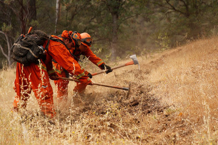 An inmate fire crew cuts fire lines in hot and smoky conditions while working to stop the spread of the Carr Fire, west of Redding, California, U.S. July 27, 2018. REUTERS/Fred Greaves