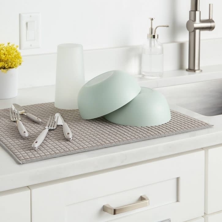 The brown drying mat on a counter with dishes on it