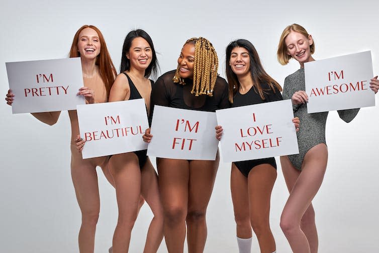 A group of female models wearing shapewear pose holding signs with body positive messages.
