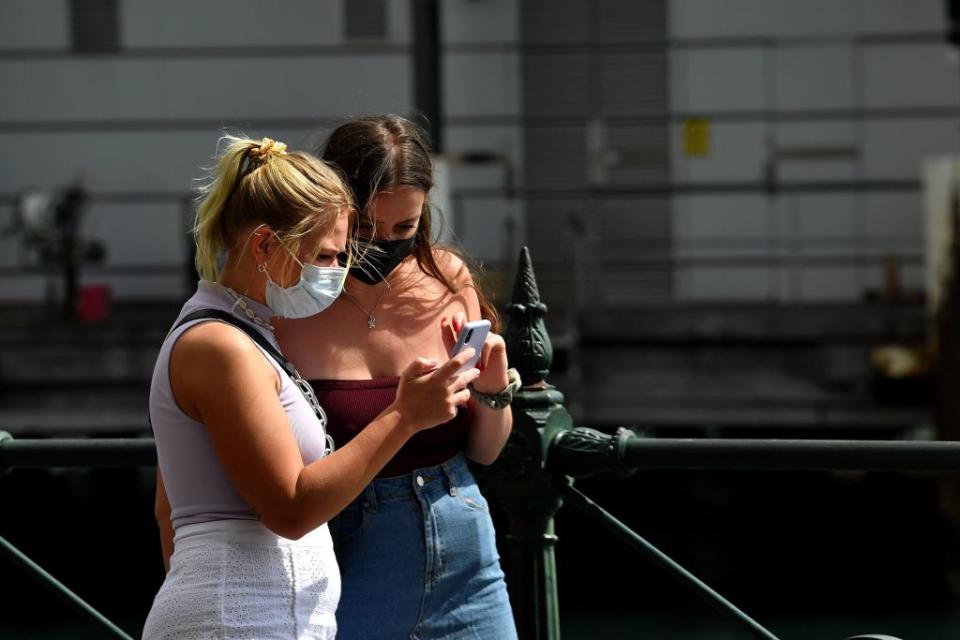 Two young women in face masks walk along a quiet Circular Quay in Sydney.