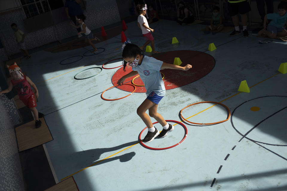 Rafaely de Melo, wearing a protective mask, jumps during gym class at the Pereira Agustinho daycare, nursery school and pre-school, after it reopened amid the new coronavirus pandemic in Duque de Caxias, Monday, July 6, 2020. The city of Manaus in the Amazon rainforest and Duque de Caxias in Rio de Janeiro’s metropolitan region, became on Monday the first Brazilian cities to resume in-person classes at private schools since the onset of the COVID-19 pandemic, according to the nation's private school federation. (AP Photo/Silvia Izquierdo)