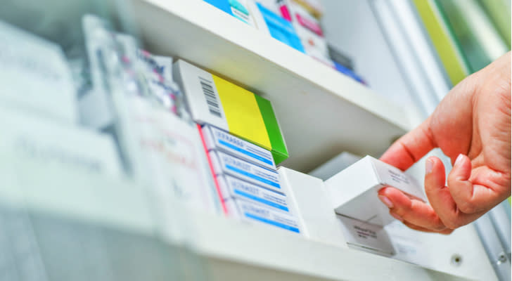 a hand grabbing a prescription from a shelf full of drugs