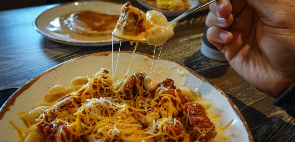 Someone eats a bowl of mac and cheese topped with Buffalo chicken