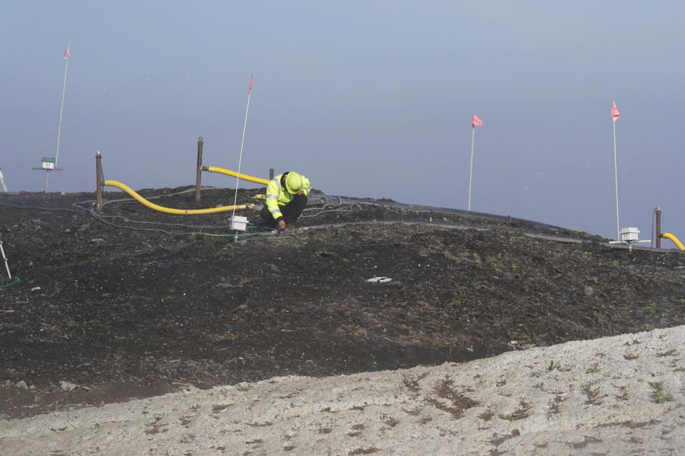 A worker inspects a composting cell at the Anaerobic Composter Facility at the Yolo County Central Landfill in Woodland, Calif., Tuesday, Nov. 30, 2021. In January 2022, new rules take effect in California requiring households to recycle excess food. The dark area is a biocover made of finished compost used to control gas emissions. The gray area is a cement, clay and fiber mixture sprayed onto the surface of the cell to seal the surface and allow for biogas capture below the cover for electricity production. (AP Photo/Rich Pedroncelli)