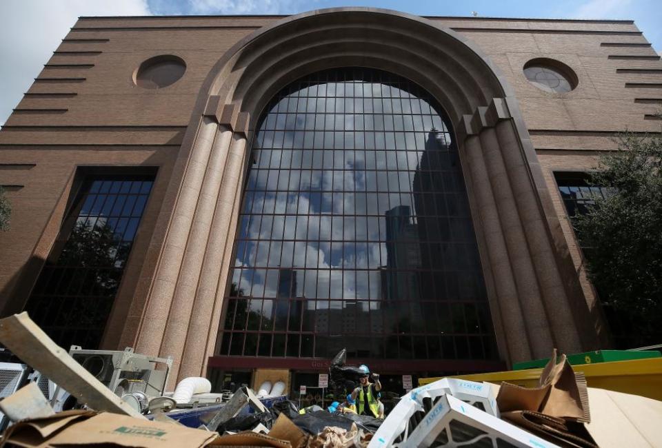 Construction workers toss bags of trash into a dumpster outside the Wortham Theater Center, which was severely damaged by flooding.