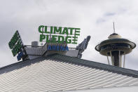 The roof-top sign for Climate Pledge Arena is shown next to the Space Needle, Wednesday, Oct. 20, 2021, ahead of the NHL hockey Seattle Kraken's home opener Saturday against the Vancouver Canucks in Seattle. The historic angled roof of the former KeyArena was preserved, but everything else inside the venue, which will also host concerts and be the home of the WNBA Seattle Storm basketball team, is brand new. (AP Photo/Ted S. Warren)