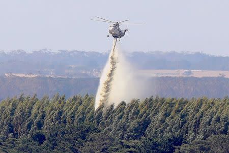 A helicopter drops water on a forest as a bushfire burns nearby, on the outskirts of the town of Cobden, located south west of Melbourne, Australia, March 18, 2018. AAP/David Crosling/via REUTERS