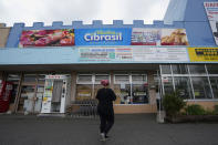 A woman walks towards a supermarket offering food, drinks and items ordinarily found in Brazil, in a town called Oizumi, about 90 kilometers (55 miles) northwest of Tokyo, Tuesday, May 31, 2022. Of Oizumi's 40,000 residents, the local city hall says 20% were born outside Japan and just over half of those are Japanese Brazilians, among the largest concentrations in Japan. (AP Photo/Hiro Komae)