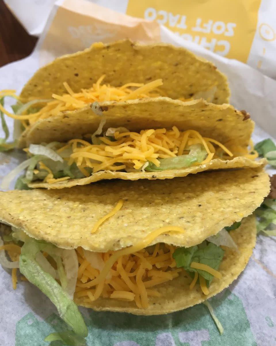 Three Del Taco value hard-shelled tacos with cheese and lettuce, selective focus, on serving paper