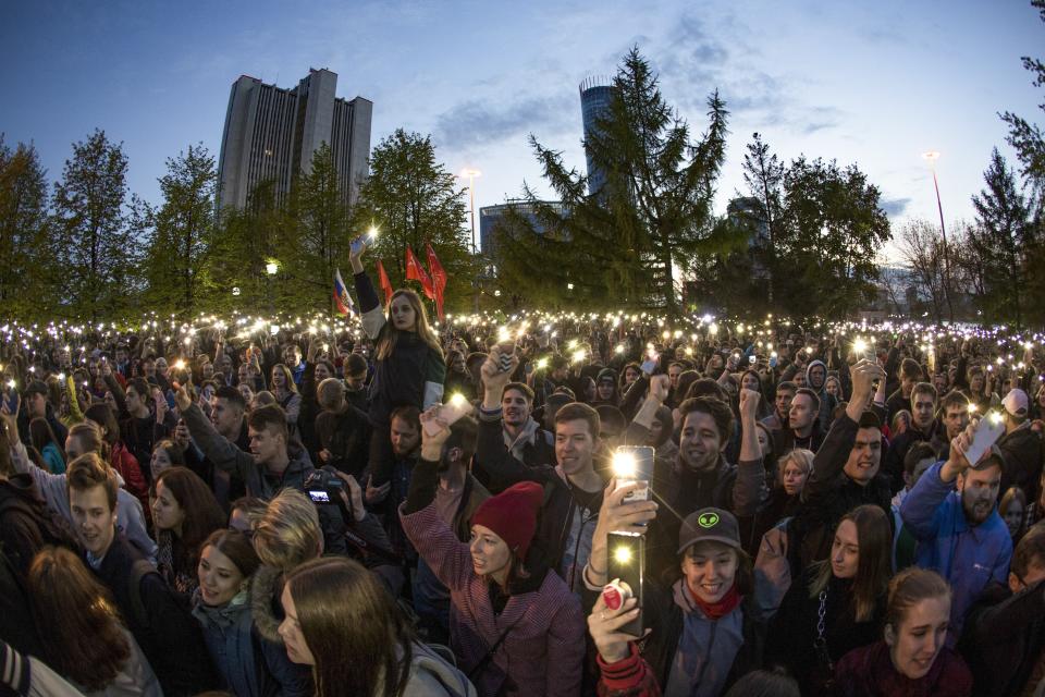 Demonstrators wave their cell phones as they gather in front of a new built fence blocked by police, during a protest against plans to construct a cathedral in a park in Yekaterinburg, Russia, Wednesday, May 15, 2019. Hundreds of riot police have surrounded a park in Russia's fourth-largest city before what's expected to be a third consecutive day of protests against building a new cathedral. (AP Photo/Anton Basanayev)