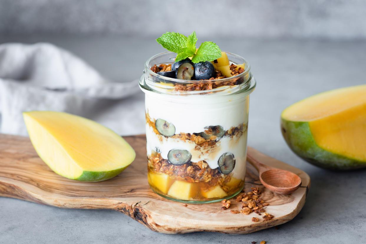 Breakfast yogurt parfait with granola, mango, berries in jar on concrete background. Concept of healthy lifestyle, healthy eating, dieting, yoga and fitness menu